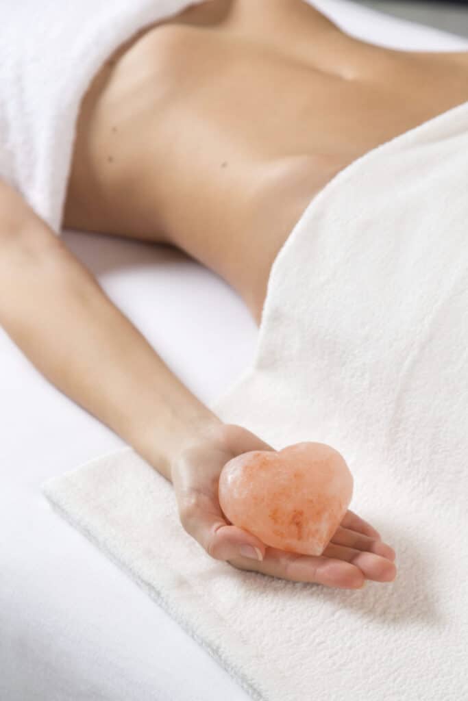 Femme allongée sous une serviette tenant une pierre de sel rose en forme de cœur