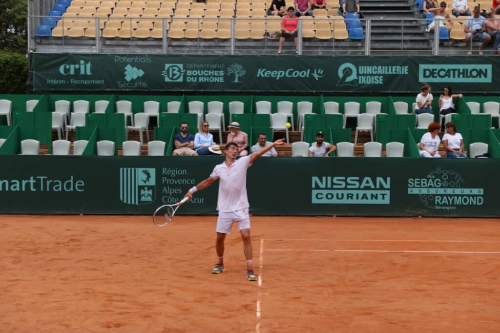 Joueur servant sur le court en terre battue de l’Open du Pays d’Aix devant les tribunes