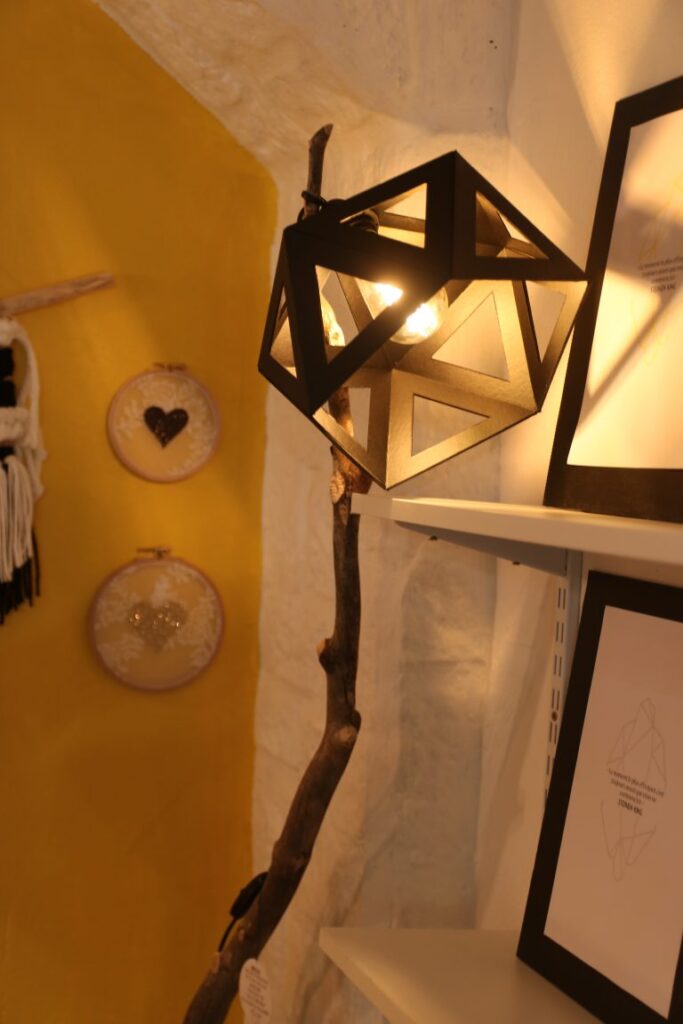 Lampe géométrique et cadres sur un mur jaune chez Aix and Co