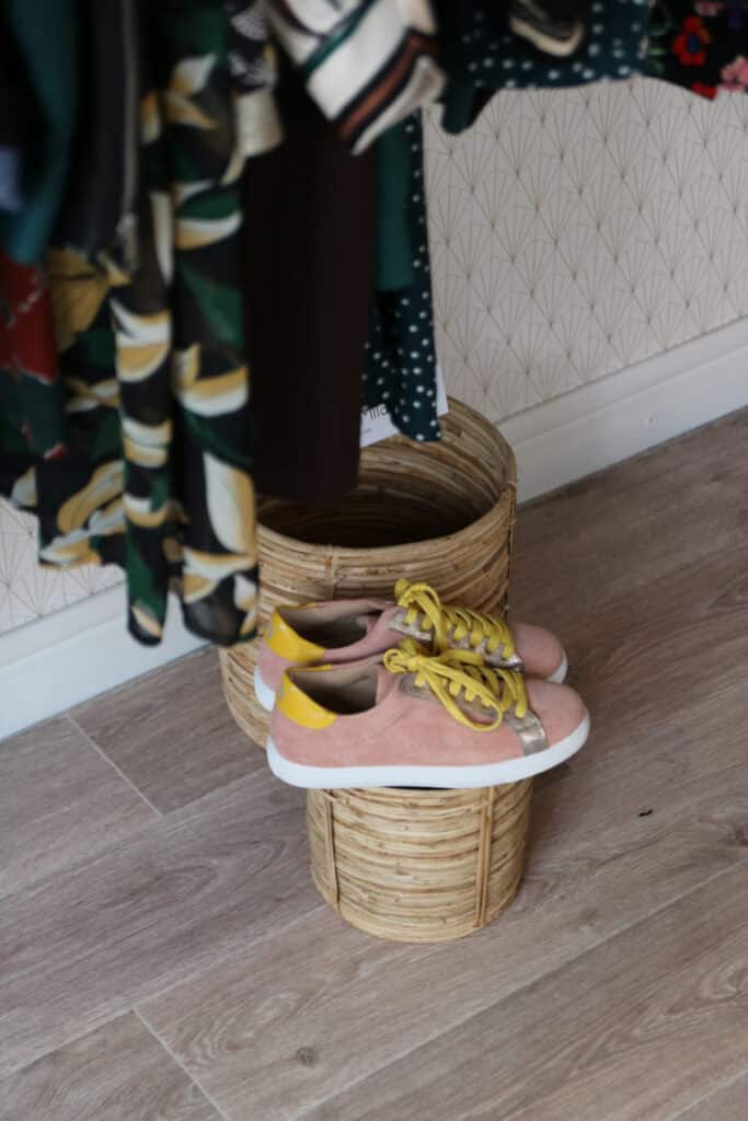 Baskets roses posées sur un panier en osier devant des vêtements chez Abbie & Lou