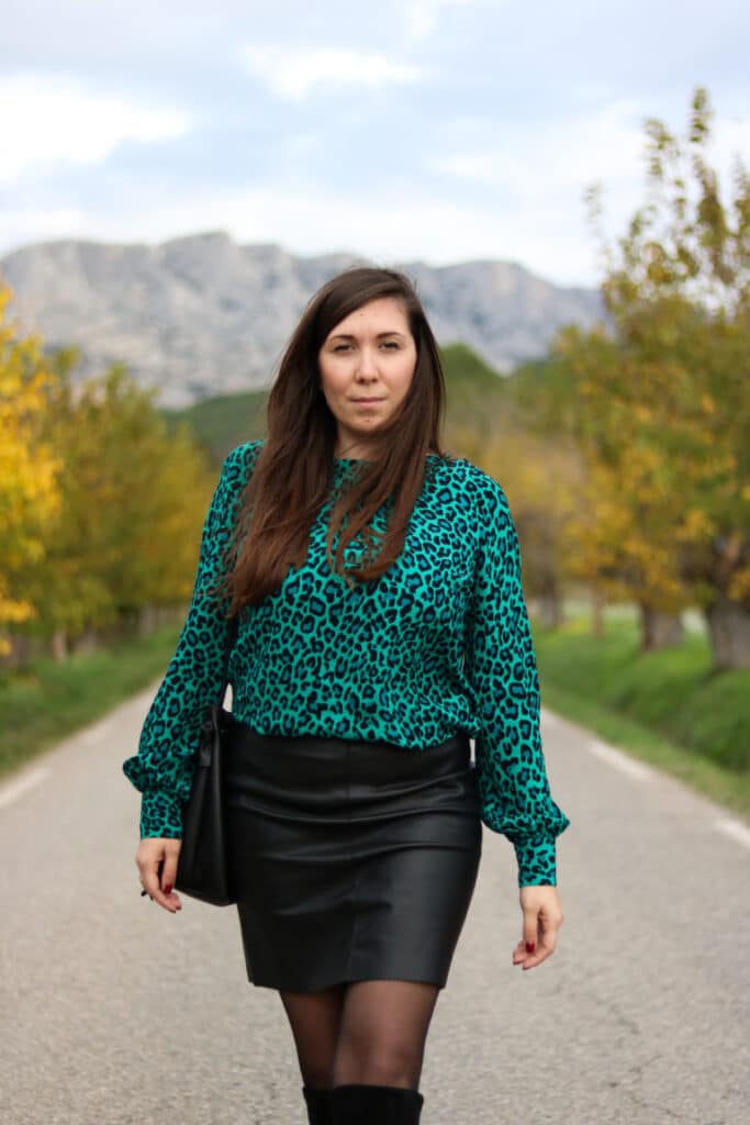 Femme en blouse verte léopard et jupe noire d’Abbie & Lou sur une route arborée