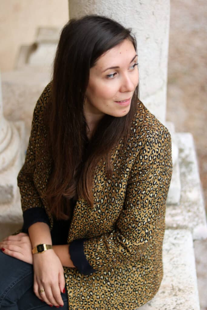 Femme en veste léopard dorée d’Abbie & Lou assise contre un mur en pierre