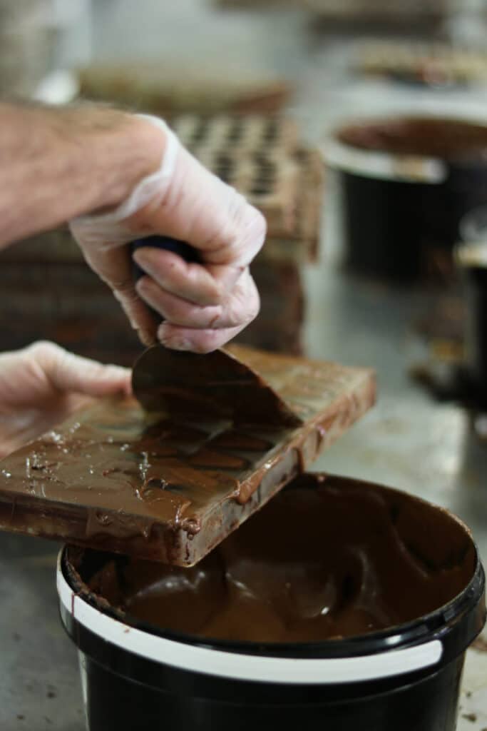 Chocolatier raclant une plaque de chocolat au-dessus d’un seau à Puyricard