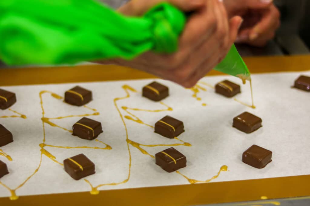 Mains décorant des chocolats d’un filet de caramel à la poche à douille