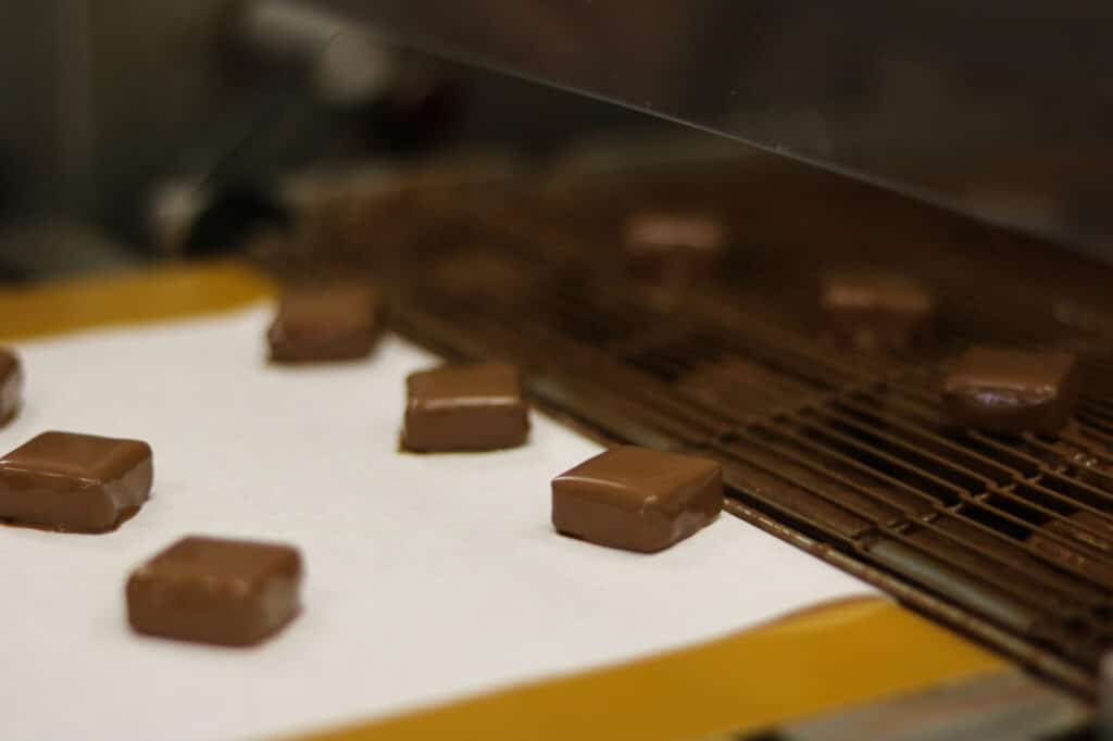 Chocolats enrobés sortant de la machine d’enrobage à Puyricard