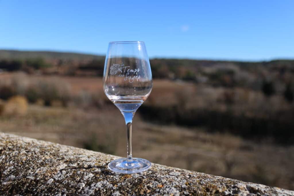 Verre de dégustation Le Temps des Sages posé sur un muret face à la campagne du Luberon
