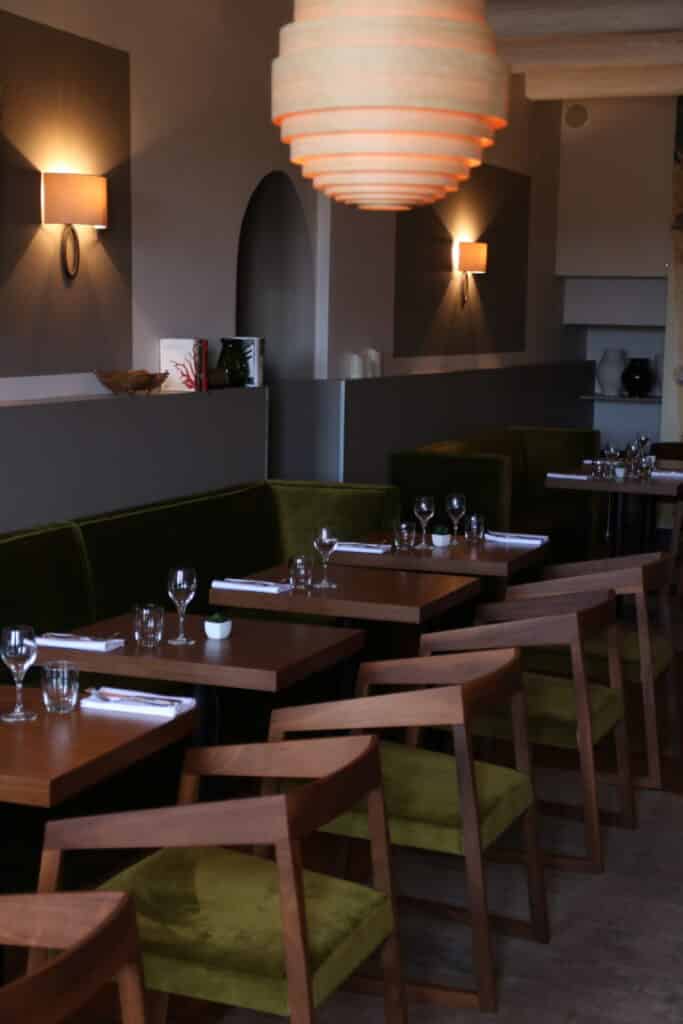 Salle du restaurant de l’hôtel Victor avec chaises en noyer et banquette verte