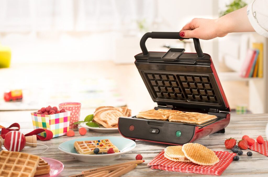 Main ouvrant le gaufrier Senya Multi Waffles entouré de gaufres et de fruits rouges