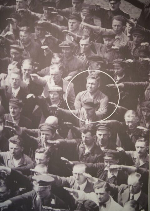 Photographie de foule avec un homme refusant de faire le salut, entouré d’un cercle